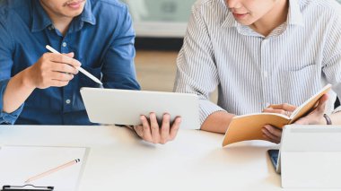 Genç iş geliştirme ekibinin iş planlarını tartıştığı / anlattığı / açıkladığı fotoğraf, düzenli çalışma odasındaki modern çalışma masasında otururken bir bilgisayar tableti ve stilus kalem kullanarak çekilmiştir..