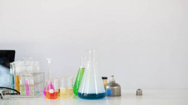 Bilimsel ekipmanlar, kimya cam eşyalar ve bilgisayar dizüstü bilgisayarı arka plan olarak beyaz çalışma masasının üzerinde beyaz çalışma masasına yerleştiriliyor..