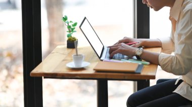 Modern ofis üzerinde ahşap çalışma masasında otururken beyaz ekran bilgisayar laptopuyla çalışan akıllı adamın kırpılmış görüntüsü..