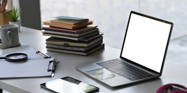 Boş ekran dizüstü bilgisayar çalışma masasına yığınla kitap, kahve fincanı, dosya, bilgisayar tableti, büyüteç koyuyor. Düzenli iş yeri kavramı.