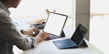 Bilgisayar tabletinde çalışan zeki bir adamın kırpılmış görüntüsü. Klavye çantasıyla birlikte masanın üzerine kitap yığını, modern ofis yerine kalem tutacağı koyuyor..