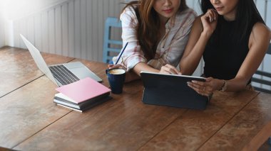 Kırpılmış çekim tasarımcısı takım toplantısı / yeni kostüm tasarımı hakkında modern ofis ile ahşap toplantı masasında otururken bir bilgisayar tableti kullanarak tartışır / konuşur.