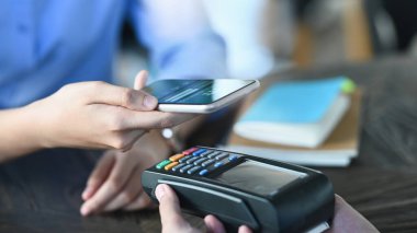 Akıllı bir adamın elinde akıllı bir telefon tutarken çekilmiş görüntüsü ve kredi kartı okuyucusunda bir NFC teknolojisi kullanarak bir ödeme yapıyor. Teknoloji ve Ödeme kavramı.