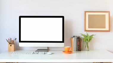 Çalışma alanı bilgisayar monitörü, beyaz çalışma masasına oturma odasındaki ofis eşyalarıyla birlikte arka plan olarak beyaz duvarı örüyor..