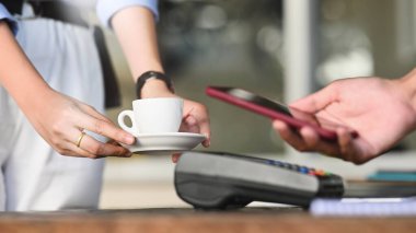 Akıllı bir adamın elinde akıllı bir telefon tutarken çekilmiş görüntüsü ve kredi kartı okuyucusunda bir NFC teknolojisi kullanarak bir ödeme yapıyor. Teknoloji ve Ödeme kavramı.