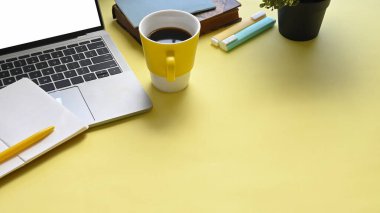 Belge, kahve fincanı, defter, kalem, keçeli kalemler ve beyaz boş ekranlı bilgisayar laptopuyla dolu renkli iş yerlerinin en üst görünümü.