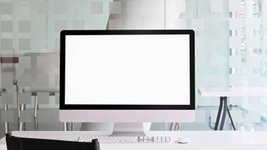 Beyaz ekranlı bilgisayar monitörünün fotoğrafı arka plan olarak kablosuz fare ve klavyeli beyaz çalışma masasına yerleştiriliyor..