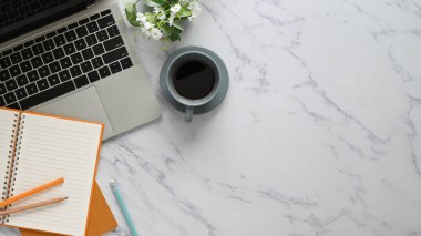 Üzerinde aksesuarlar olan mermer masanın üst görünümü. Düz dizüstü bilgisayar, seramik kahve fincanı saksı bitkisi, defter ve kalem. Düzenli / Rahat iş yeri konsepti.