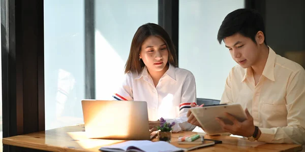 Photo of young business developer team discussing/meeting/working with computer laptop and tablet while sitting together at wooden working desk over orderly living room as background.