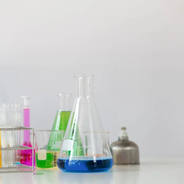 科学仪器和化学玻璃器皿放在实验室白墙上方的白色工作台上作为背景的照片 — 图库照片