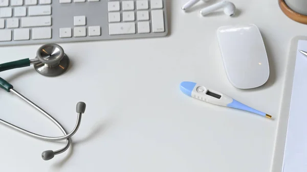 白い現代の机の上に医療用具の写真 フラットレイアウト聴診器 マウス キーボード デジタル温度計 クリップボードやワイヤレスイヤホン 現代と秩序のある医師の職場の概念 — ストック写真