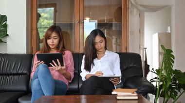 Asyalı kadınlar siyah deri koltukta bilgisayar tabletiyle oturup dinleniyorlar..