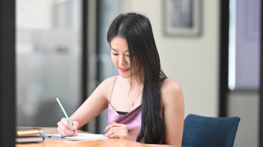 Güzel bir kadın ahşap çalışma masasında notlar alıyor..