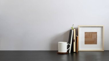 Arkaplan olarak beyaz beton duvar ile birlikte kitap, defter ve resim çerçevesiyle birlikte çalışma masası. Düzenli çalışma alanı kavramı.
