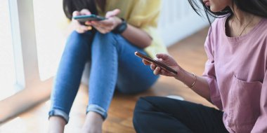 Akıllı telefonlarıyla rahatlarken rahat oturma odasının üzerinde yan yana oturarak rahatlayan güzel kadınların görüntüsü..