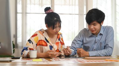 Grafik tasarım ekibi ahşap çalışma masasında bilgisayar tableti ve evrak işleriyle uğraşıyor..