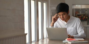 Beyaz gömlekli adam, arka plan olarak lüks ve modern oturma odasının üzerinde çalışırken bilgisayar üzerine yoğunlaştı..