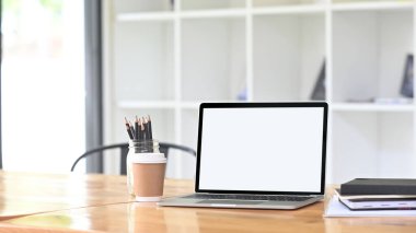 Beyaz ekran bilgisayar dizüstü bilgisayar ve ofis ekipmanlarıyla çevrili rahat bir çalışma alanı.