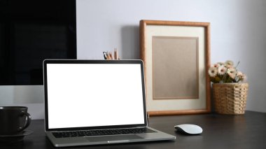 Siyah çalışma masasının fotoğrafı, beyaz boş ekran bilgisayar dizüstü bilgisayar, kitaplar, defter, kalem tutucu, resim çerçevesi, arkaplan olarak beyaz çimento duvarlı bir saksı..