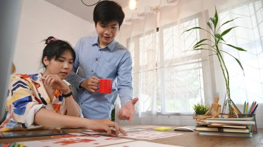 Grafik tasarım ekibi ahşap masada bir bilgisayarla çalışıyor..