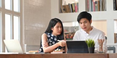 Evde çalışan genç bir ofis çalışanının fotoğrafı. İş çifti, ahşap masada rahat oturma odasının üzerinde yan yana oturuyor..