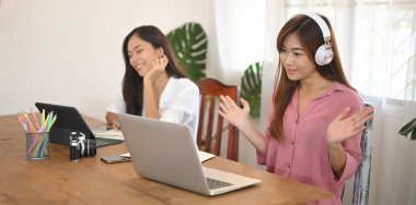 Kadınlar tahta masada yan yana otururken bilgisayar tableti ve dizüstü bilgisayar kullanıyorlar..