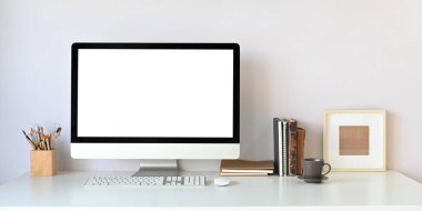 Beyaz beyaz ekranlı bilgisayar monitörü beyaz çalışma masasına koyuyor. Etrafı kalem tutacağı, fare, klavye, kitaplar, kahve fincanı ve resim çerçevesiyle çevrili..