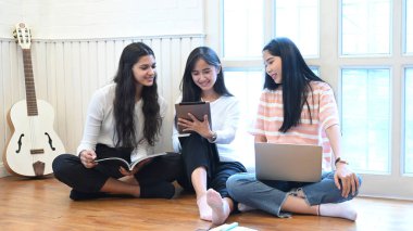 Üç kadın, oturma odasının ahşap zemininde otururken rahatlıyor ve konuşuyorlar..