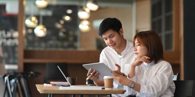 Genç çift, arka plan olarak rahat bir kafe üzerinde ahşap masada otururken bilgisayar laptopu ve belgeyle birlikte çalışıyorlar..