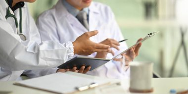 Doktor olarak çalışan iki zeki adamın elinde bir tablet ve pano tutarken düzenli bir çalışma ortamı olarak doktor masasında oturup tartışırken ve yan yana otururken çekilmiş görüntüsü..