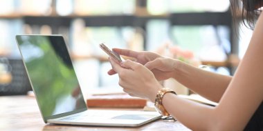 Kırpılmış bir kadının görüntüsü bilgisayarın önünde otururken akıllı telefon kullanıyor..