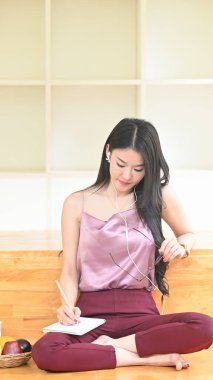 Genç bir Asyalı kadın rahat oturma odasında otururken not alıyor..