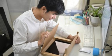 Akıllı bir adam, beyaz çalışma masasında online alışveriş yaparken bir karton kutuyu açıyor..