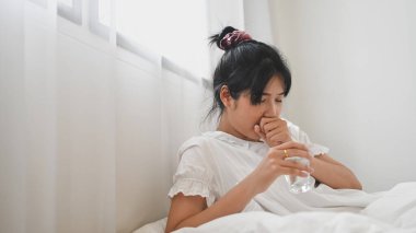 Hasta bir kadın yatak odasında yatakta yatarken su içip hap içiyor..