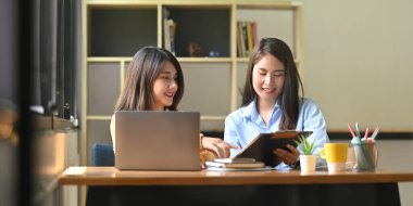 Kadınlar, ahşap çalışma masasında dizüstü bilgisayar ve panoyla birlikte çalışıyorlar..