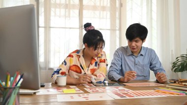 Grafik tasarım ekibi ahşap çalışma masasında bilgisayar tableti ve evrak işleriyle uğraşıyor..