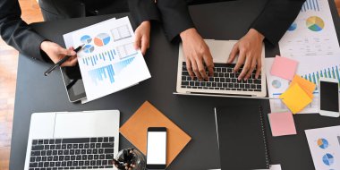 İşletme yöneticilerinin iş planlarını bilgisayar ve grafik grafikleriyle tartışırken modern ofisin üzerinde siyah toplantı masasında yan yana oturmaları..