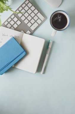 Rahat bir işsapının üst görüntüsü. Bilgisayar dizüstü bilgisayarı, sıcak kahve fincanı, kalem, defter, günlük, vazodaki çiçekler çalışma masasının üzerinde duruyordu..