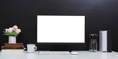 Beyaz ekran bilgisayar monitörü ve çeşitli ekipmanlarla çevrili konforlu bir çalışma alanı.