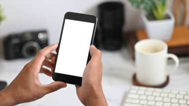 Arka planda beyaz beyaz ekranlı akıllı telefonu, kahve fincanını ve ofis ekipmanını tutan el resimleri var. Düzenli çalışma alanı kavramı.