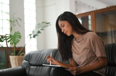 Bir kadın siyah deri bir koltukta otururken bilgisayar tableti ve stil kalem kullanıyor..