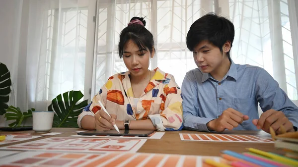 Grafik tasarım ekibi ahşap çalışma masasında bilgisayar tableti ve evrak işleriyle uğraşıyor..