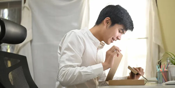 A smart man is unboxing a cardboard box from shopping online at the white working desk.