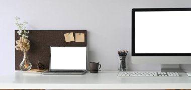 Masada ofis ekipmanlarıyla birlikte beyaz boş ekran dizüstü bilgisayar ve bilgisayar monitörü 