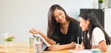 Genç bir anne kızına tahta masada ödev yapmayı öğretiyor..