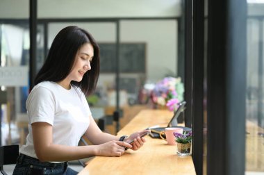 Güzel bir kadın ahşap tezgahta otururken akıllı telefon kullanıyor..