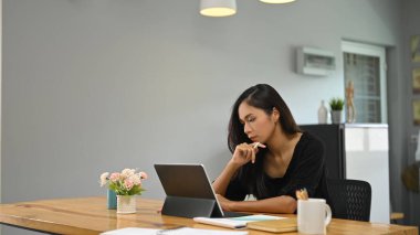 Genç bir kadın tahta bir masada otururken bilgisayar tableti kullanıyor..