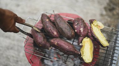 Kömür ocağında patates kızartmak için maşa kullanan el.
