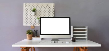 beyaz ekranlı bilgisayar beyaz çalışma masasında kitaplık, kablosuz fare, klavye, kahve fincanı, saksı bitkisi ve kitap yığını 