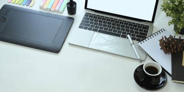 Kahve fincanı, laptop, tablet ve diğer ofis ekipmanları beyaz çalışma masasında. 